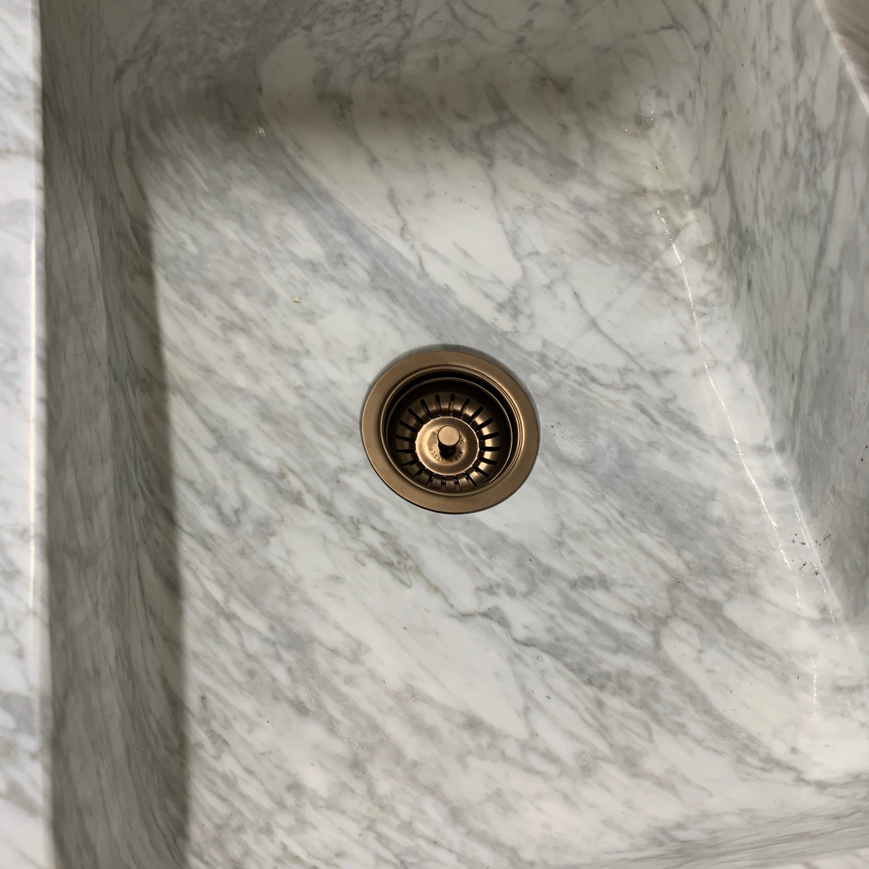 A single-sized marble butler sink with a mirror finish, featuring a central drain and a brass fixture.